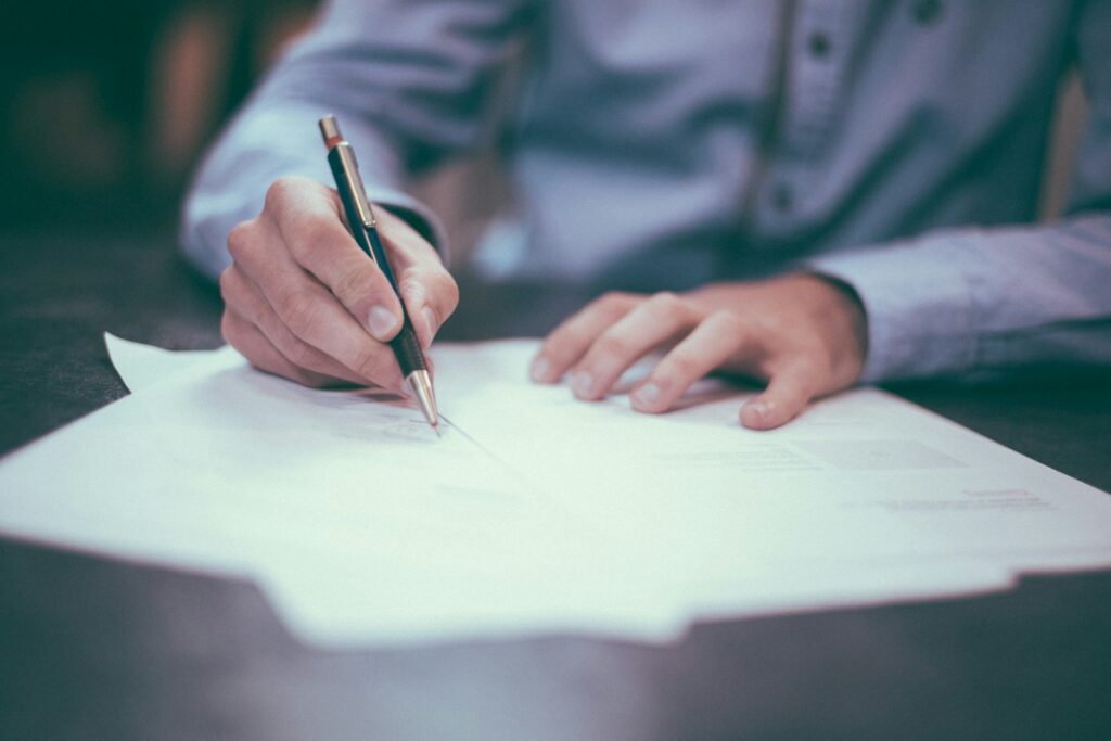 Hand mit Stift beim Ausfüllen eines Dokuments am Schreibtisch, symbolisch für das Arbeitszeugnis