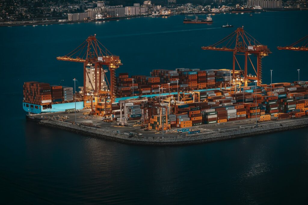 Containerschiff und Kräne in einem Hafen bei Nacht als Bild für Welthandel und Konjunkturdaten