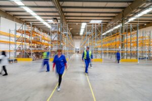 Mitarbeitende im Gang eines Hochregallagers – Lagerprozesse, die beim ERP-Wechsel weiterlaufen müssen