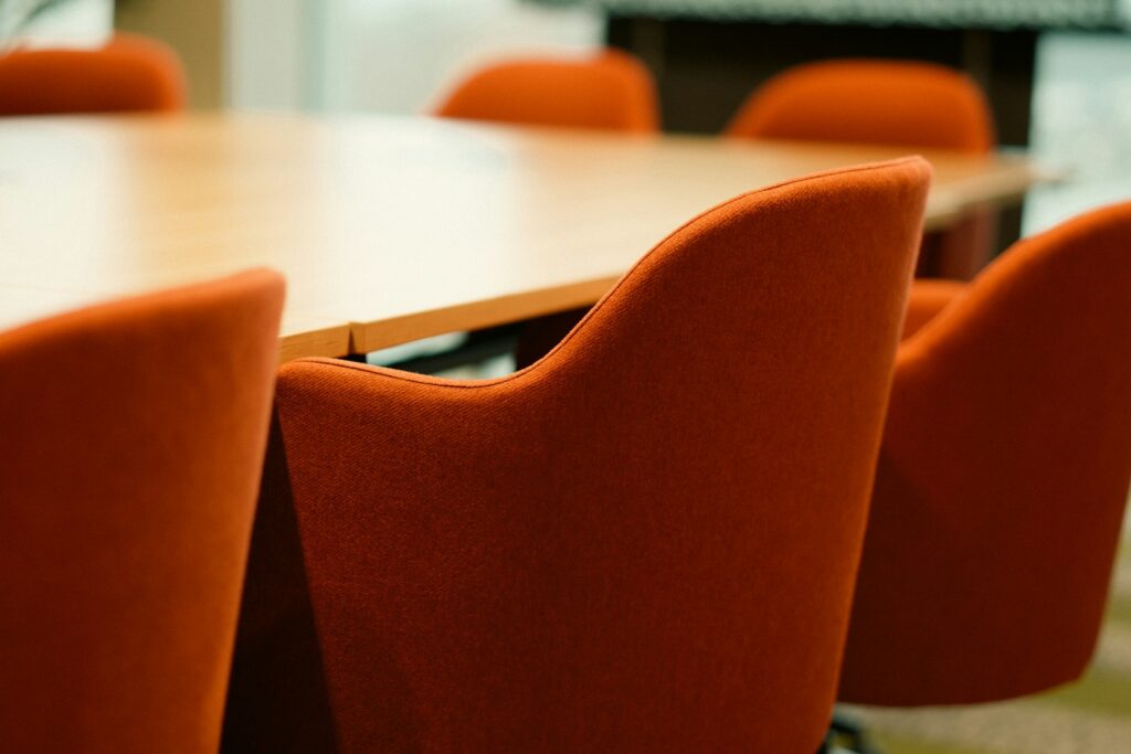 Leerer Konferenzraum mit orangefarbenen Stühlen – hier fällt die Entscheidung für oder gegen Mittelstandsanleihen