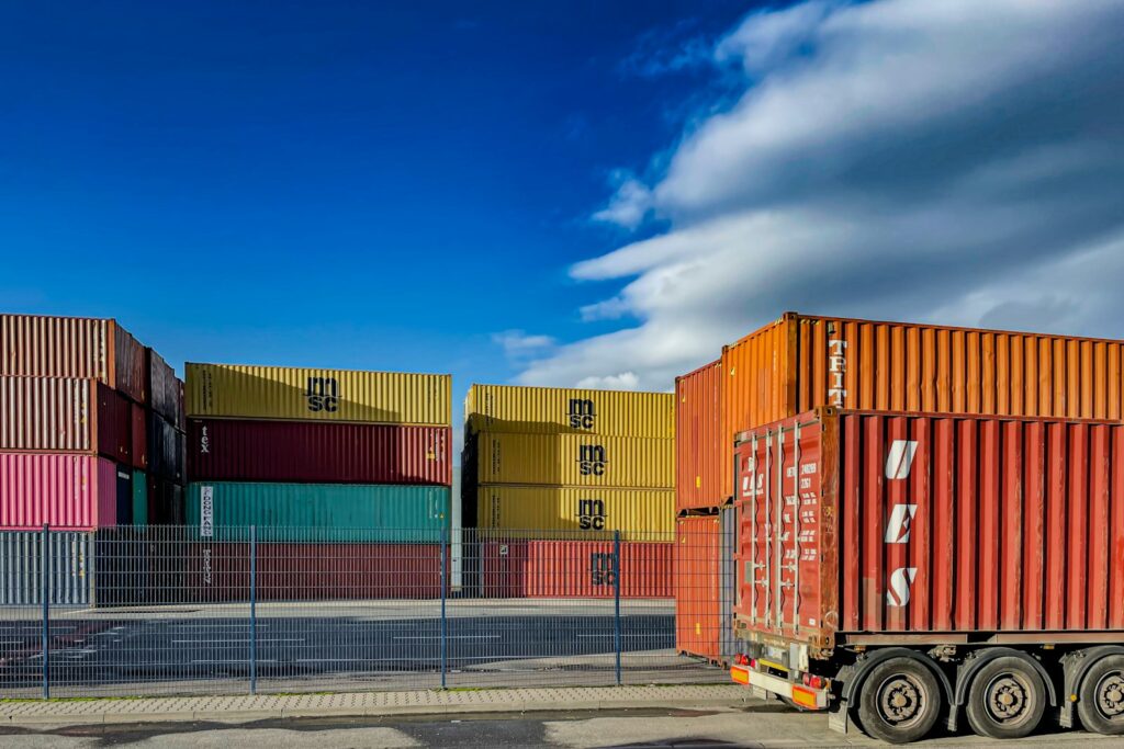 Nearshoring und Logistik: Lkw vor gestapelten Schiffscontainern auf einem Containerterminal